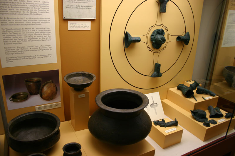 Radbeschläge, Küchengeräte, Urnen und verschmorte Bronzeteile aus dem Fürsten-Wagengrab Hart (ca. 1200 v. Chr.)